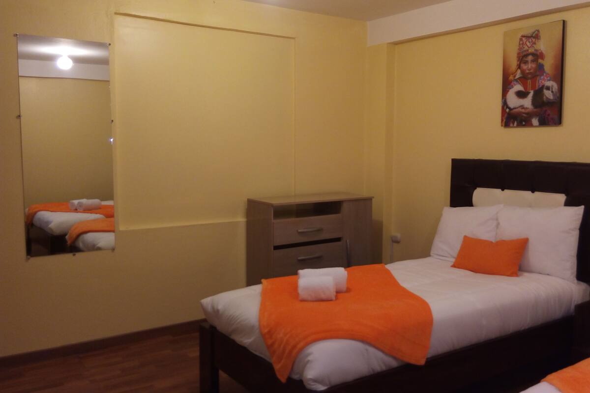 A hotel room with a bed, a dresser, a nightstand, a red lamp, and a painting on the wall.