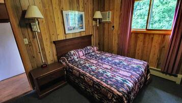 A wooden-paneled room with a bed, two wall-mounted lamps, a picture, and a window with curtains.