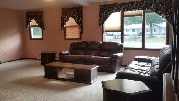 A living room with a leather sofa, a wooden coffee table, a TV on a wooden stand, and a window with curtains. - Red Ranch Motel (Catskill)