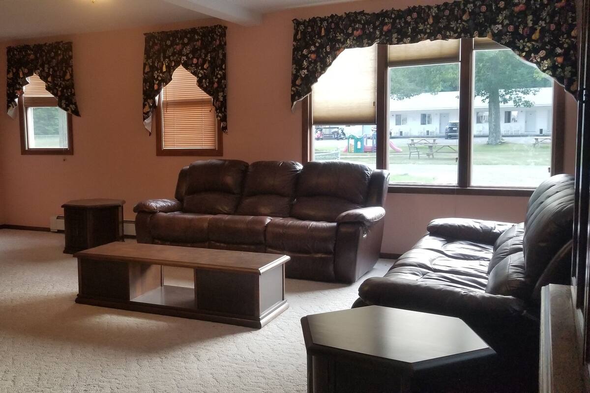 A living room with a leather sofa, a wooden coffee table, a TV on a wooden stand, and a window with curtains.