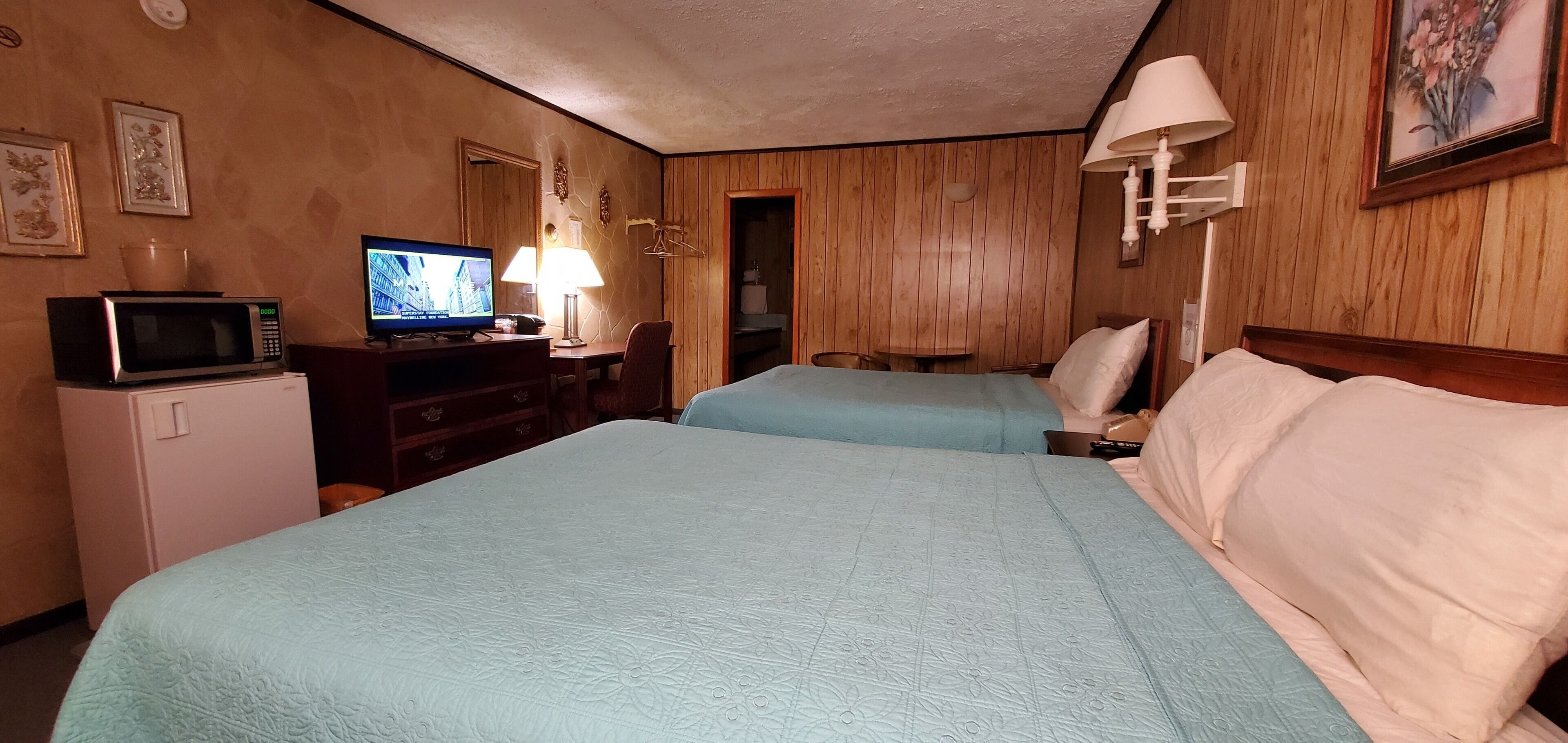 A hotel room with two beds, a television, a desk with a lamp, and a microwave.