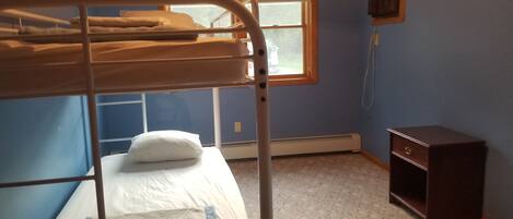 A bunk bed with a white mattress and a pillow, a small wooden nightstand, and a window with blinds.