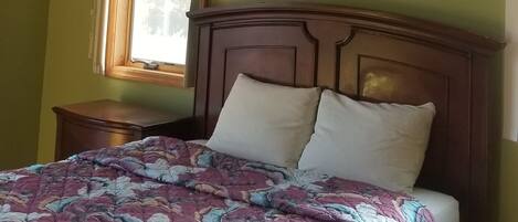 A bedroom with a sloped ceiling, a skylight, a bed with a patterned quilt, a wooden headboard, and a nightstand.