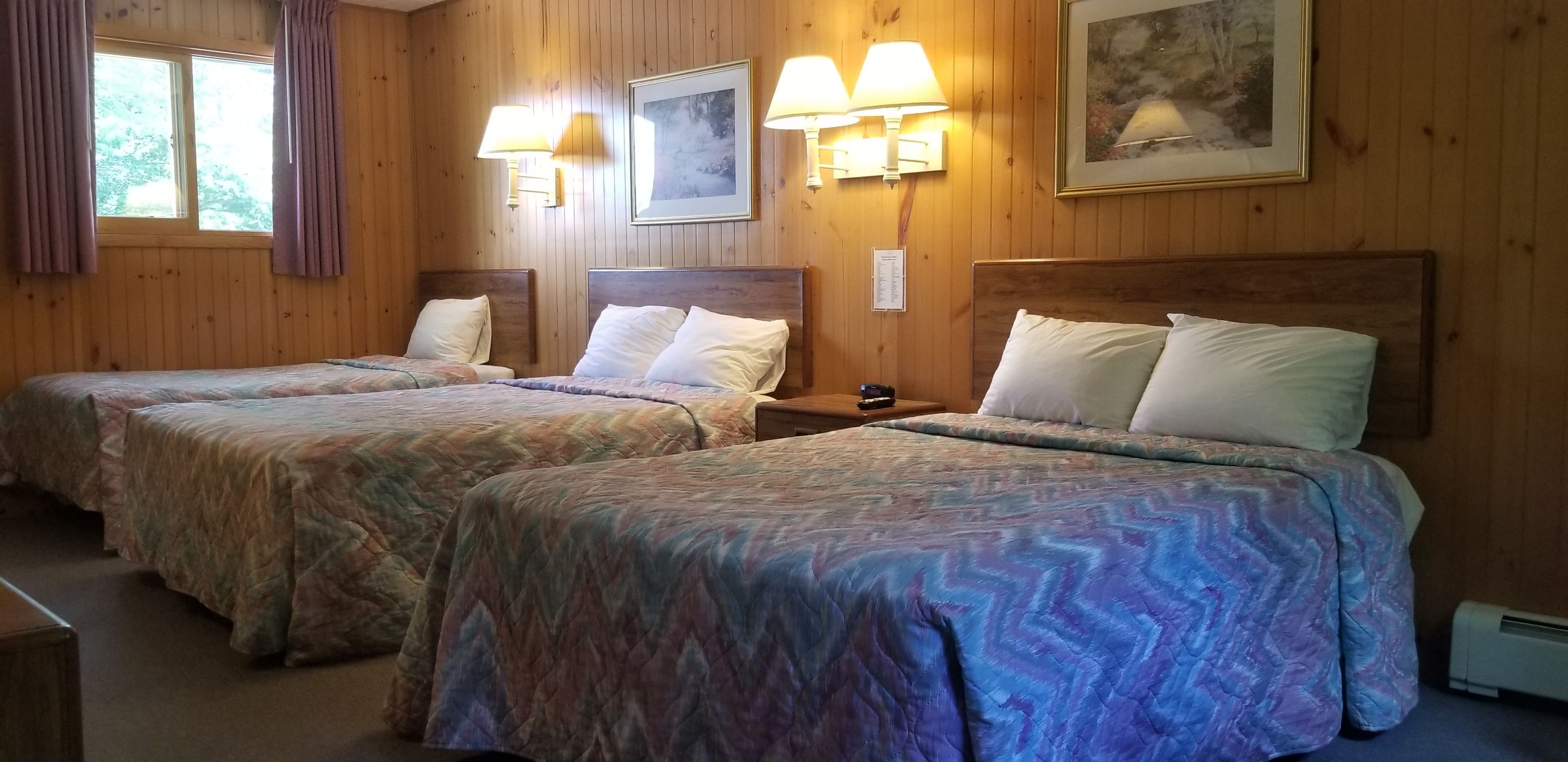A room with two beds, wooden walls, and wall-mounted lamps.