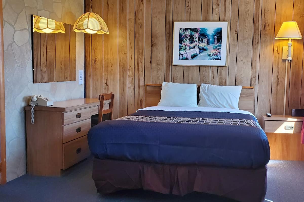 A wooden-paneled bedroom with a bed, bedside tables, a dresser, and a painting on the wall.