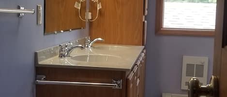Un baño con tocador de madera, lavabo, espejo y ventana.