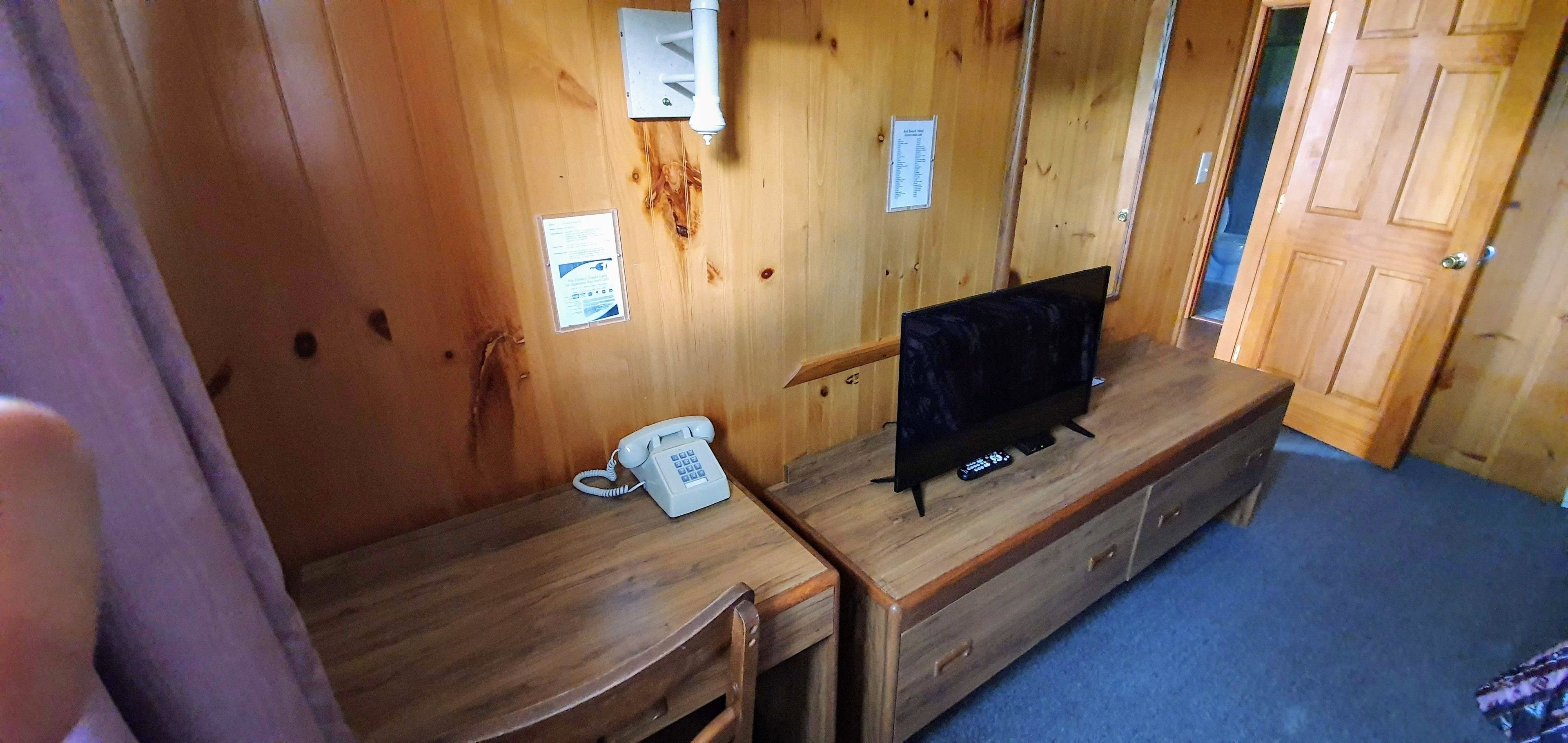 A wooden interior with a wooden desk, a telephone, and a television on a wooden stand.