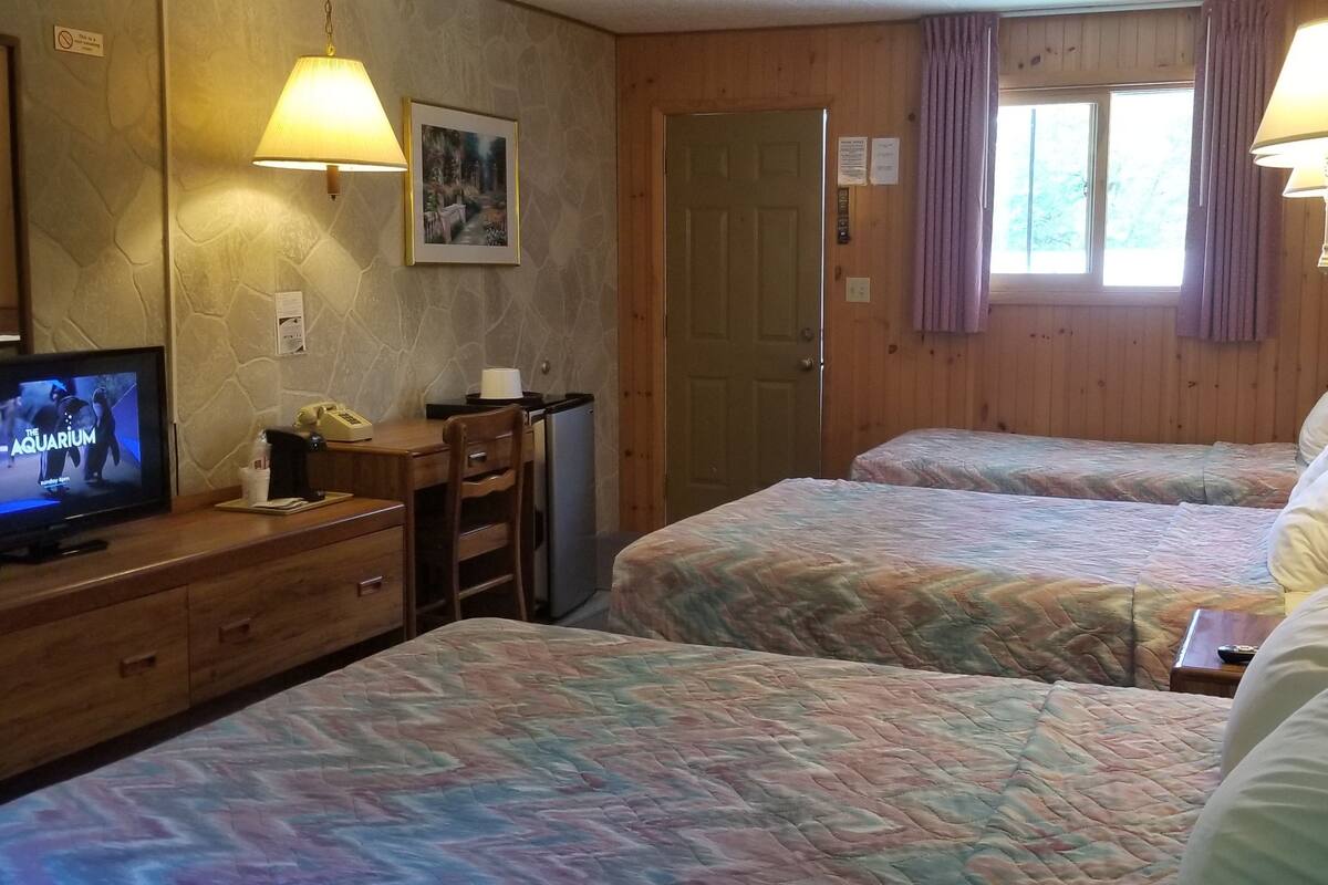 A hotel room with two beds, a television, a desk with a chair, and a window with curtains.