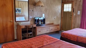 A hotel room with two beds, a wooden dresser, a television, and a stone wall. - Red Ranch Motel (Catskill)