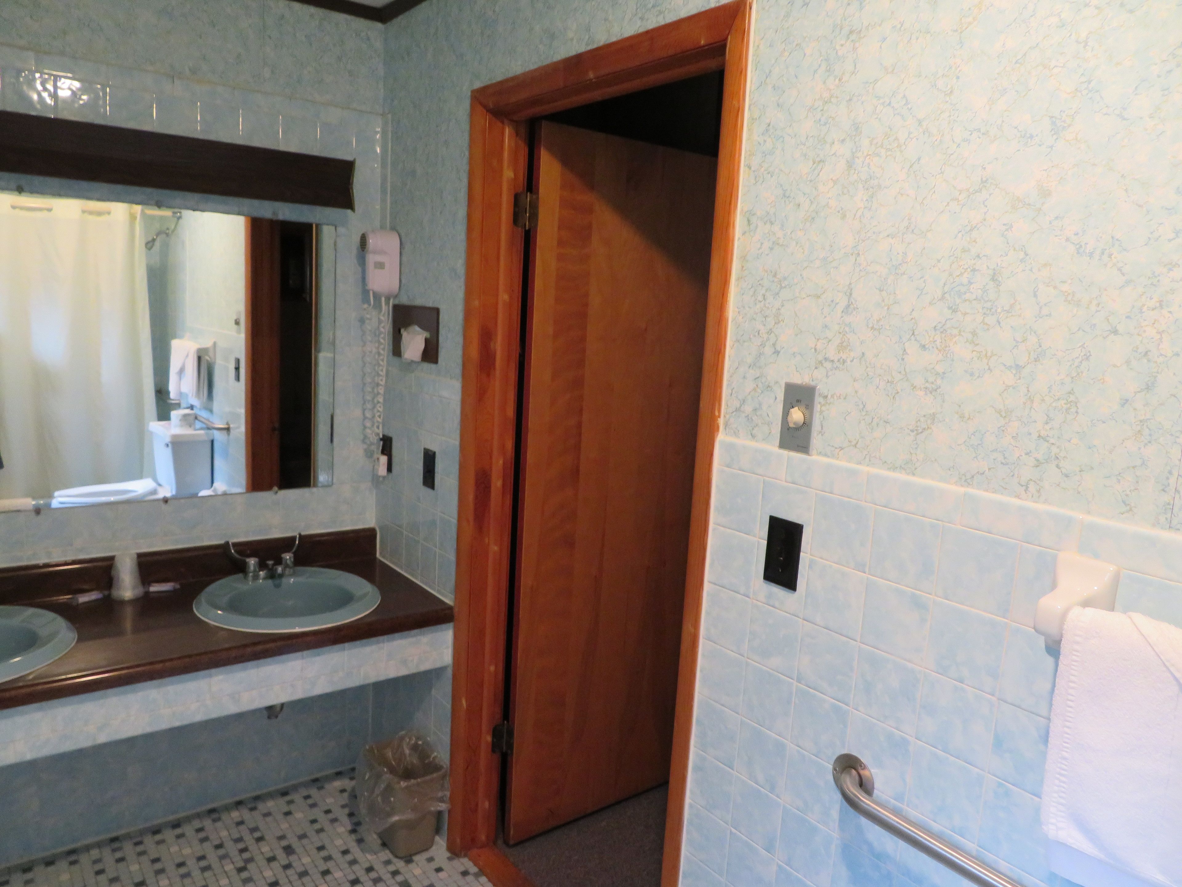 Uma casa de banho com porta de madeira, pia, espelho e um porta-toalhas.