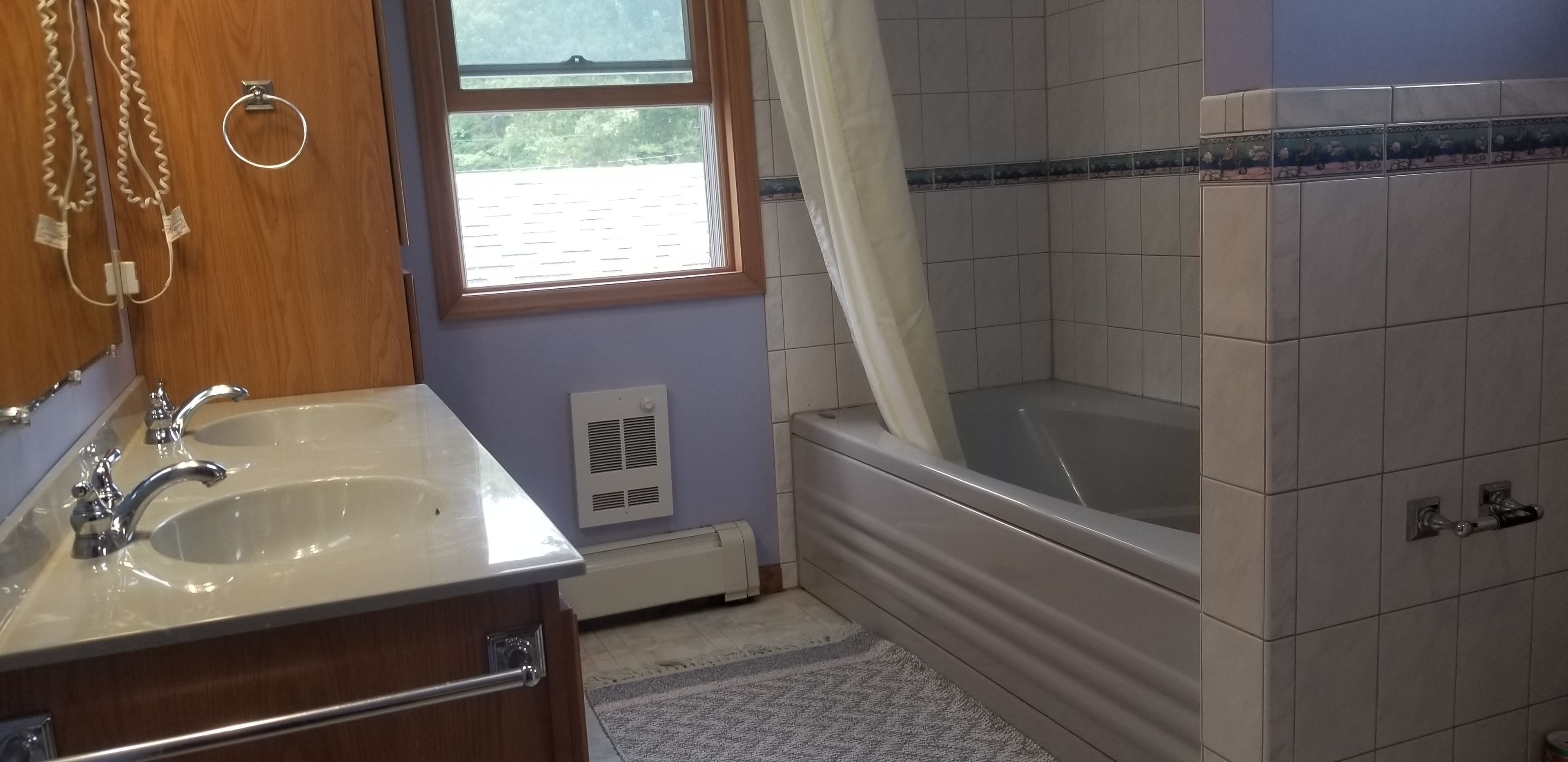 A bathroom with a sink, vanity, bathtub, and a window with a view of the outside.
