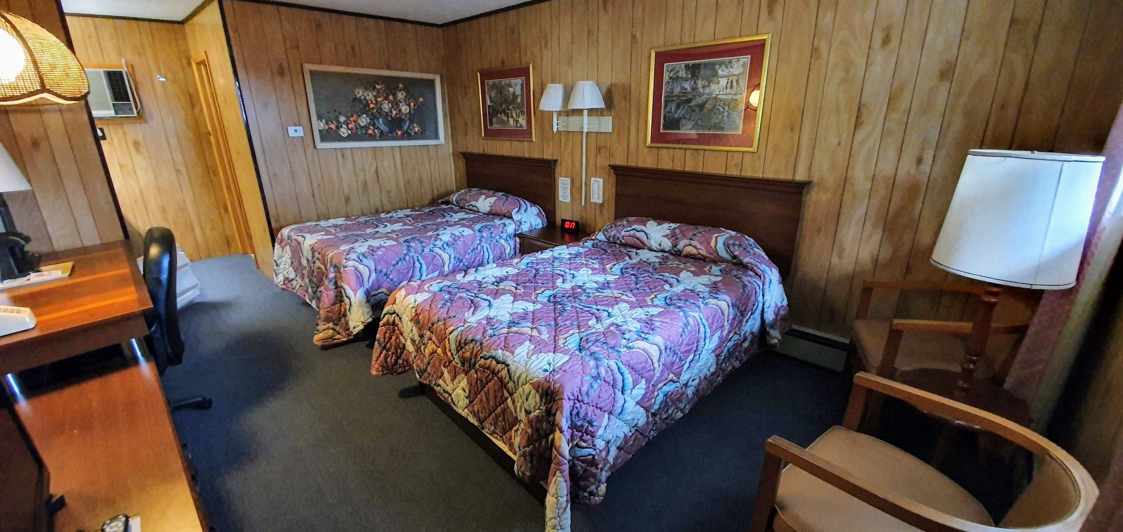 Habitación de hotel con dos camas, paneles de madera, un escritorio, una silla y una lámpara.