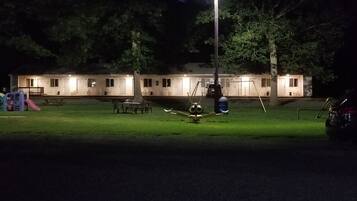 A row of motel rooms with a grassy lawn in front, a swing set, and a car parked nearby.
