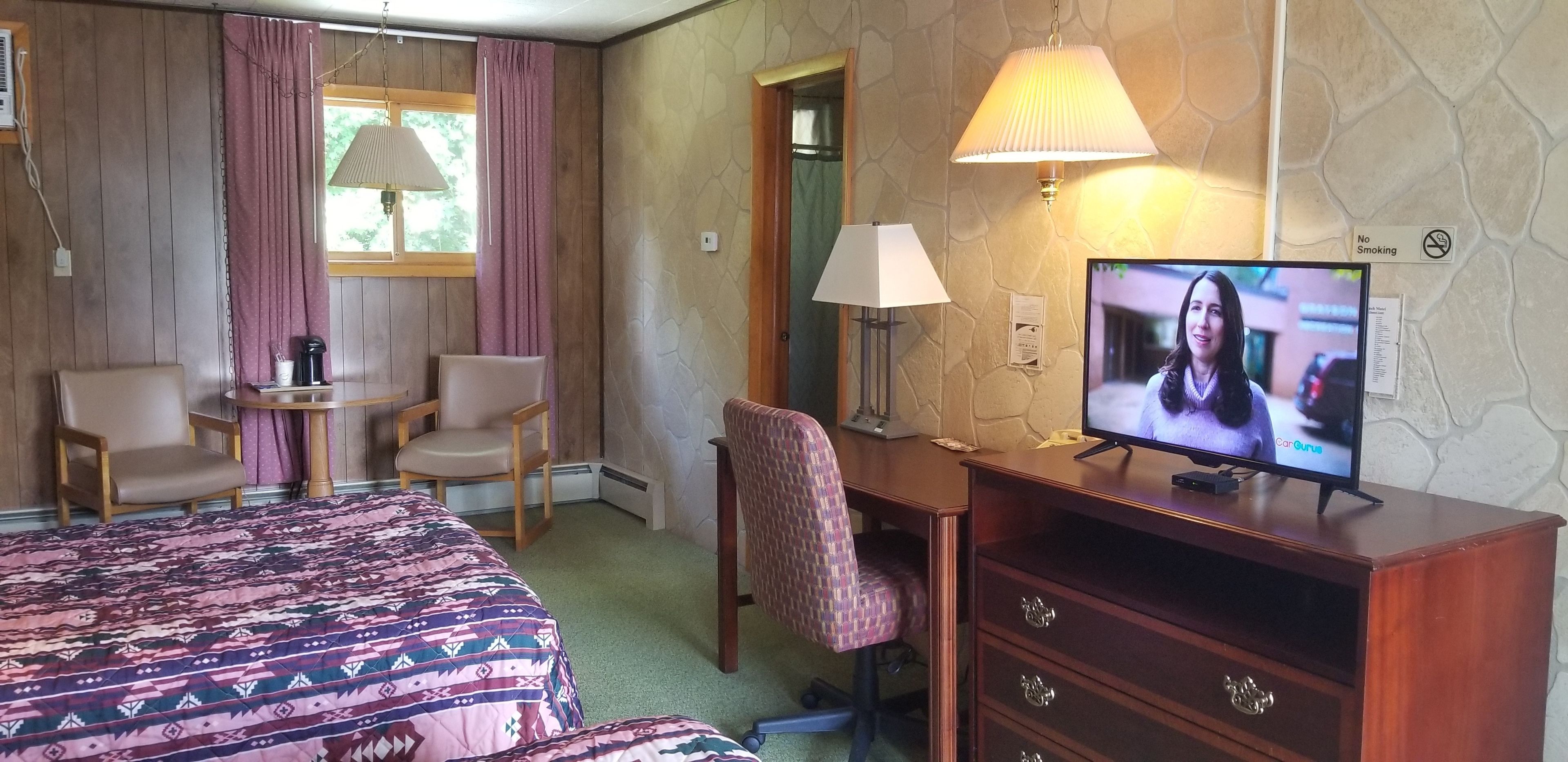Habitación de hotel con cama, dos sillas, escritorio con televisor y lámpara.