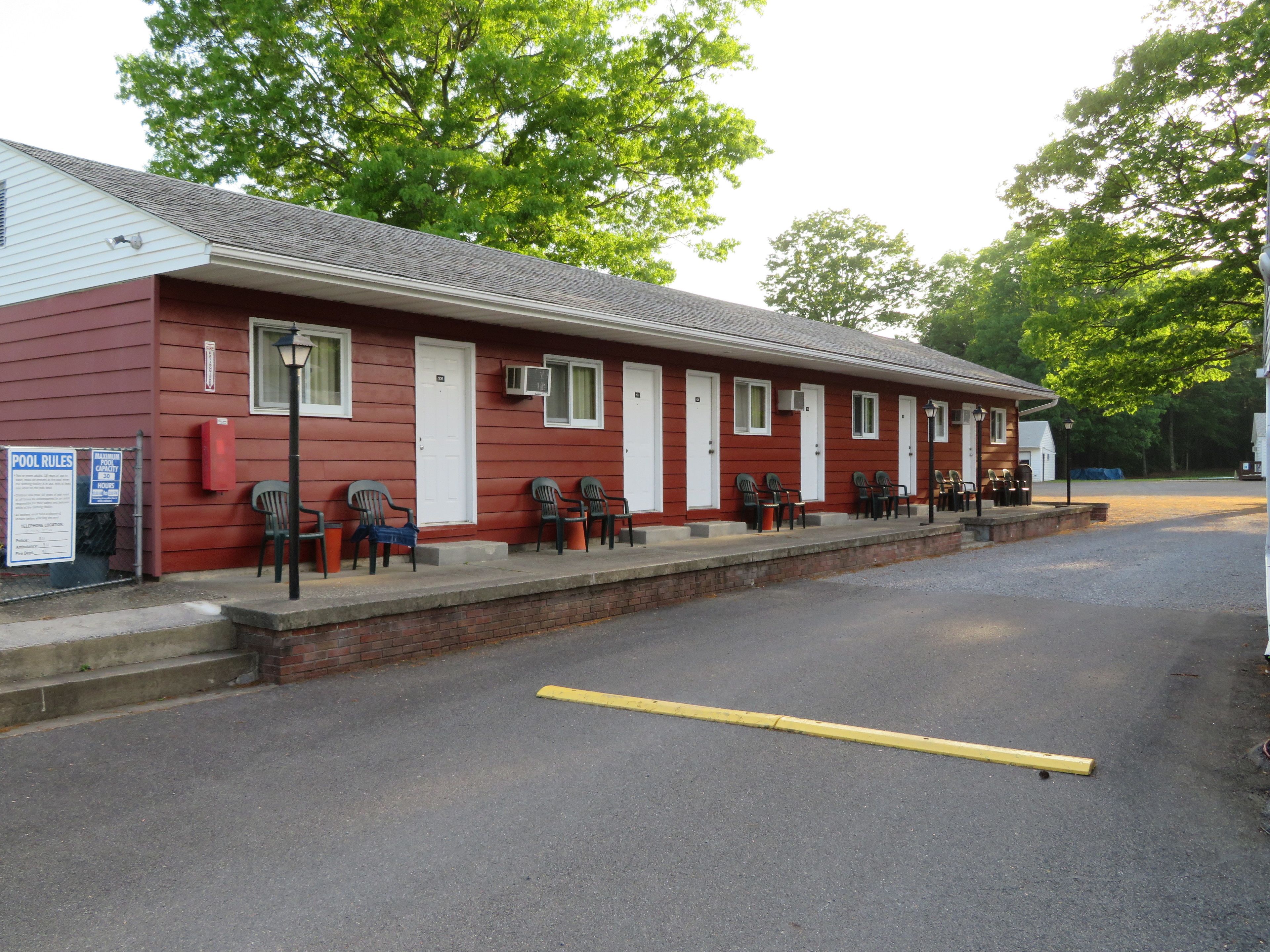 A red motel with multiple rooms, a covered outdoor seating area, and a parking lot.