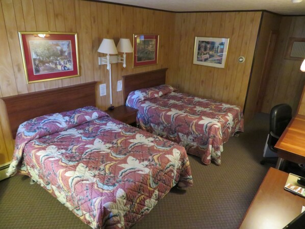 Una habitación con dos camas, paredes de madera y un escritorio con una silla.