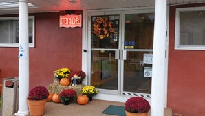A storefront with a 'DEFACE' sign, a 'NO PETS' notice, and various seasonal decorations including pumpkins and flowers. - Red Ranch Motel (Catskill)