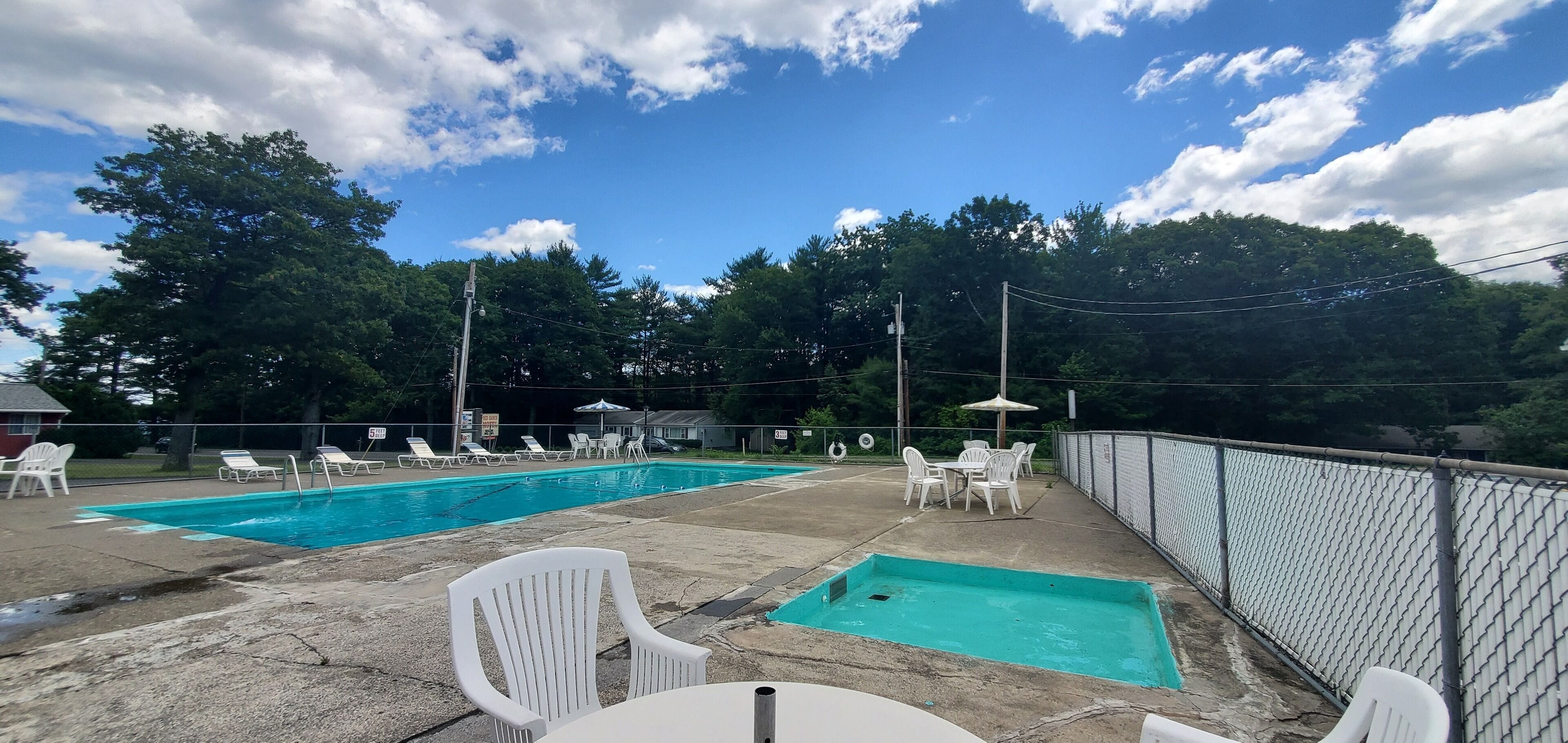 A backyard with two swimming pools, lounge chairs, and a table.