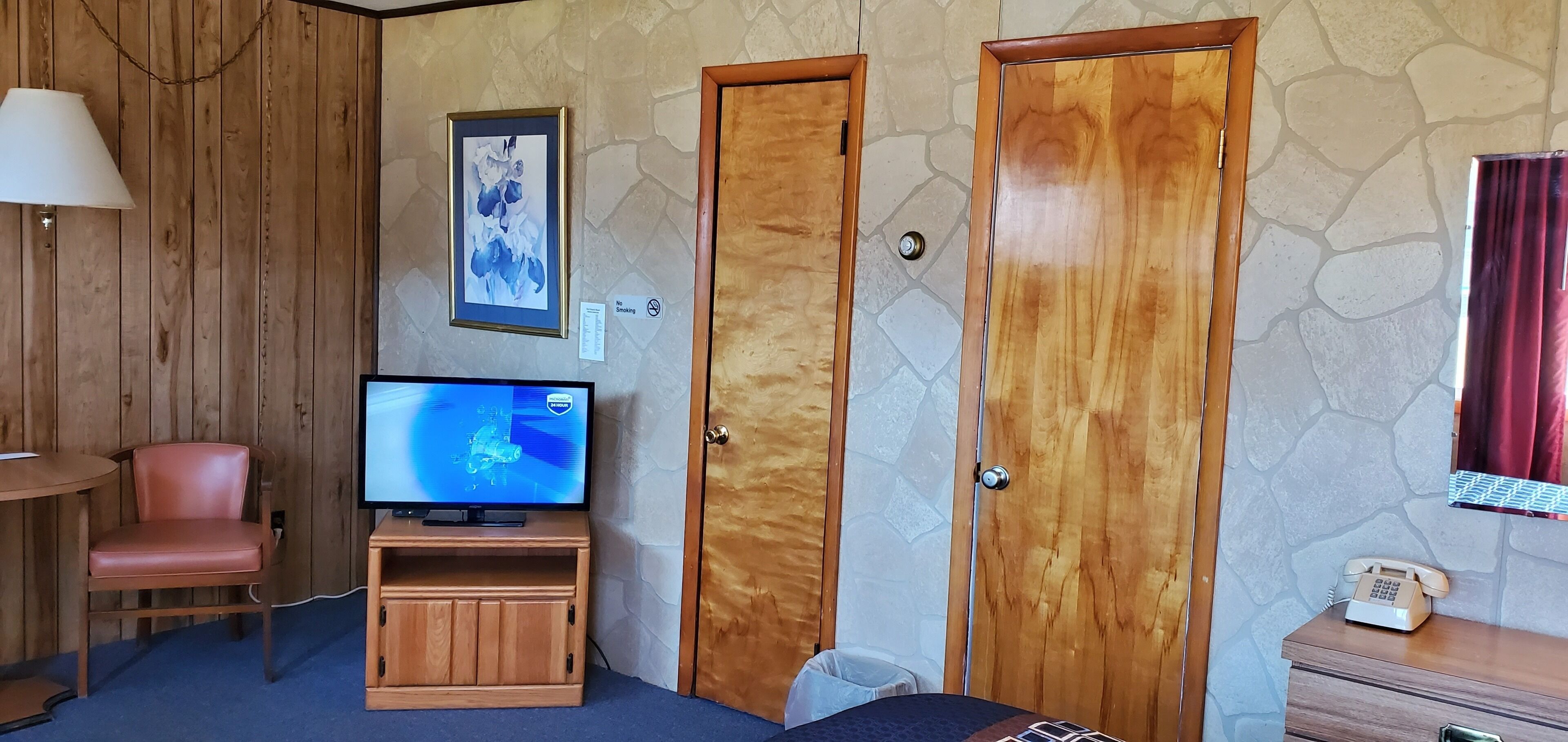 A room with a television on a wooden stand, a chair, a wooden wardrobe, and a stone-patterned wall.