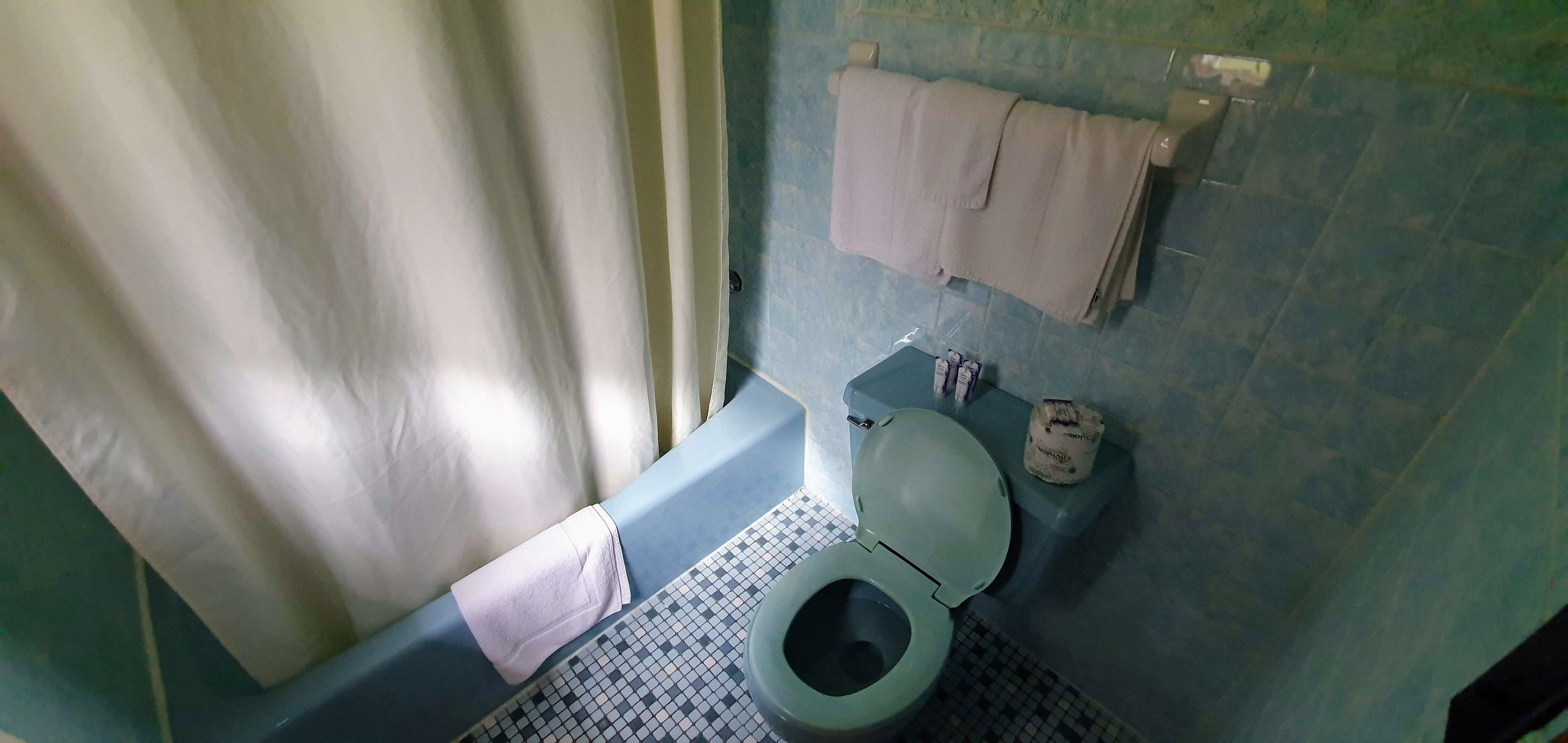 Een badkamer met een toilet, een klein prullenbakje en een handdoekrek met handdoeken.