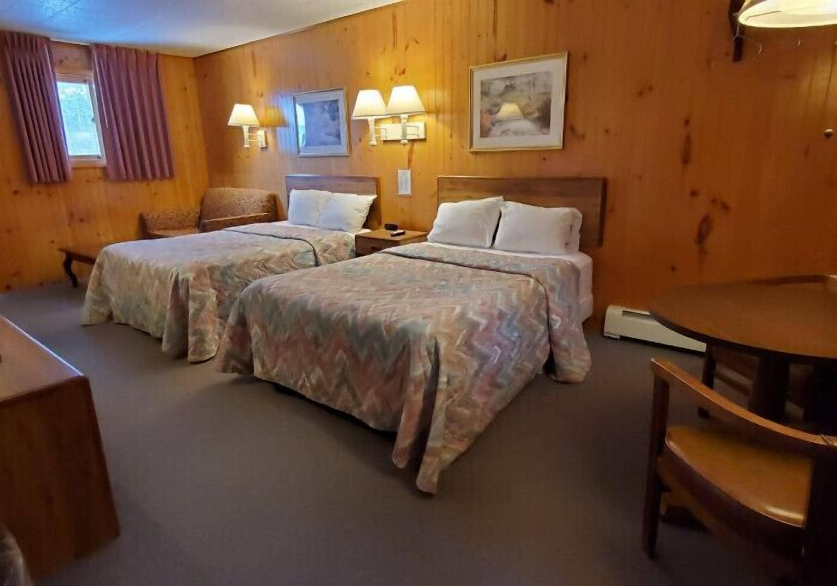 A room with two beds, wooden walls, a round table, and a bench.