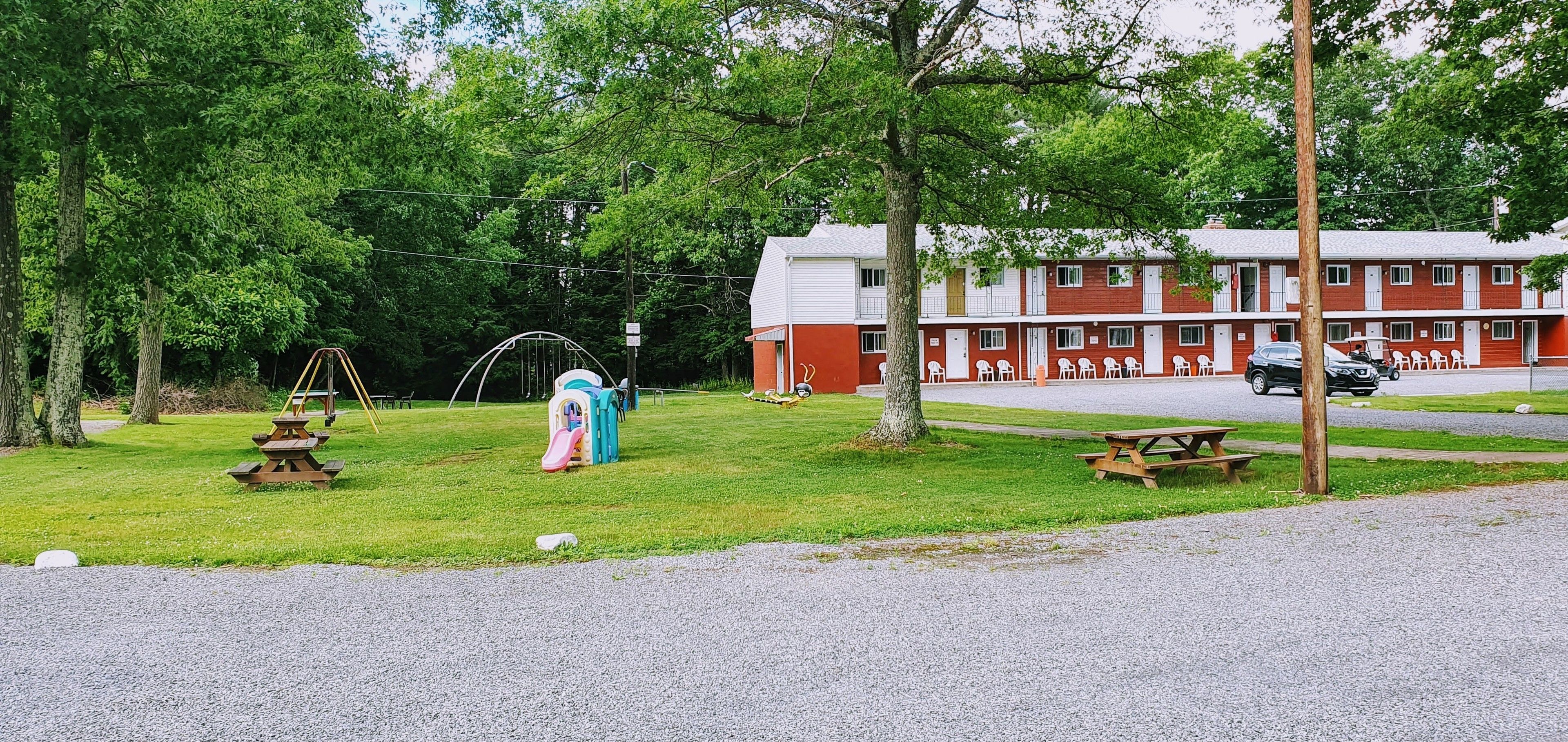 A motel with a red and white exterior, picnic tables, a playground, and a parking area.