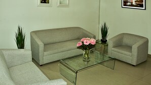 A living room with a grey sofa, a glass coffee table, and two armchairs. There are two framed pictures on the wall and a vase with flowers on the coffee table. - Riviera Hoteles Ejecutivo (Arequipa)