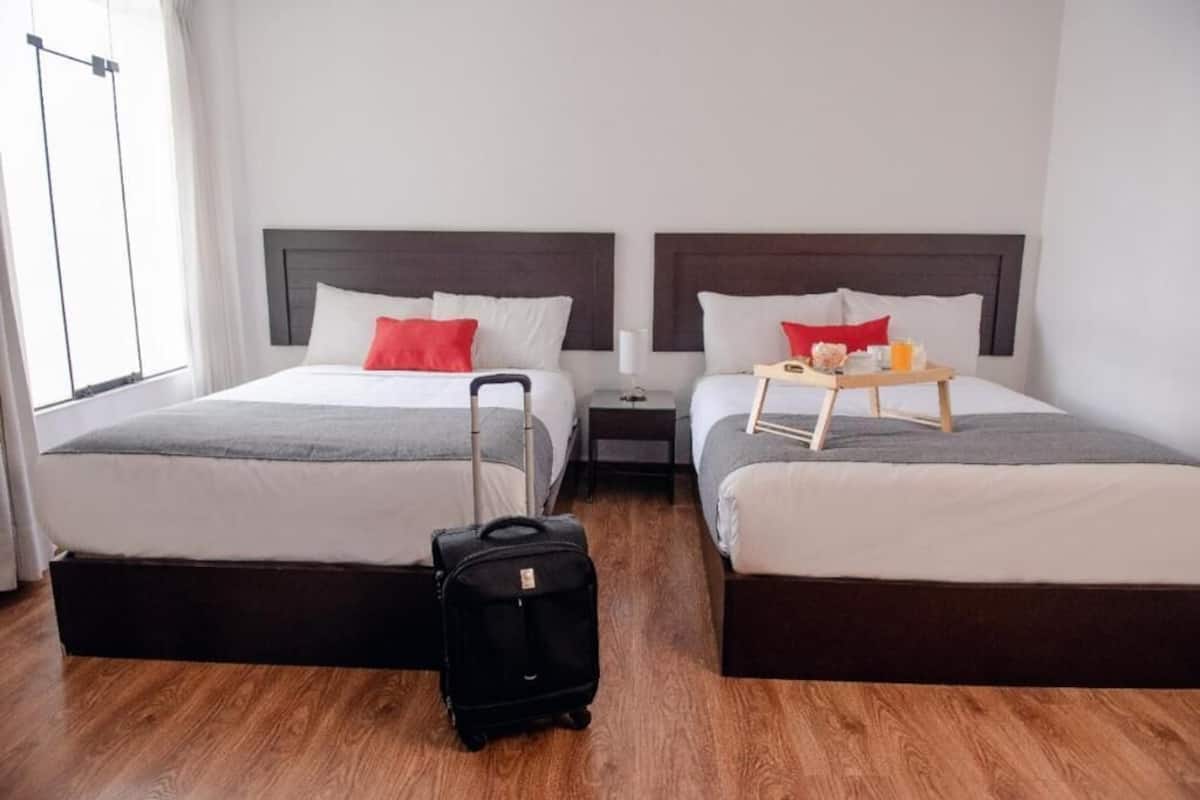 A hotel room with two beds, a wooden floor, a suitcase, and a tray table with breakfast items.