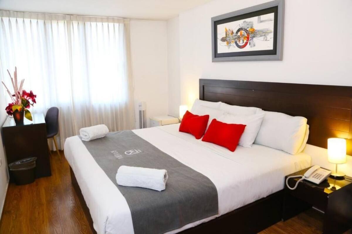 A hotel room with a large bed, a desk, a chair, a telephone, and a framed picture on the wall.