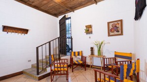 Una habitación amplia con una escalera de madera, varias sillas con cojines a rayas, una pequeña mesa con un florero y un cuadro en la pared.