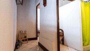 Un pasillo estrecho con suelo de baldosas, un banco de madera, una pequeña mesa con un reloj y una cortina amarillo brillante.