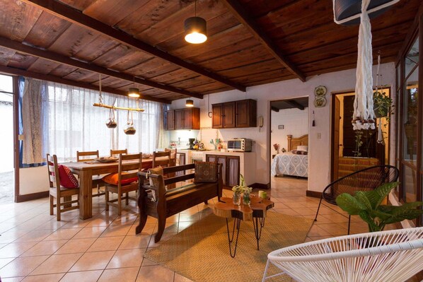 Une cuisine chaleureuse avec des meubles en bois, un coin repas avec une table et des chaises en bois, et un salon avec un canapé et un fauteuil blanc.
