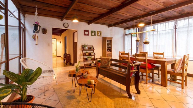 Un salón acogedor con techo de madera, un sofá, una mesa de comedor con sillas y una estantería.