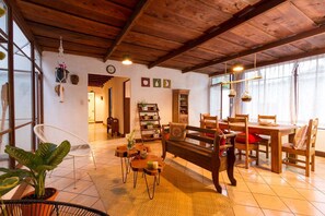 A cozy living room with a wooden ceiling, a sofa, a dining table with chairs, and a bookshelf. - Tamarindo Guest House (Antigua Guatemala)