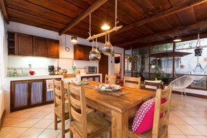 Una mesa de madera con sillas, una zona de cocina con armarios y luces colgantes.