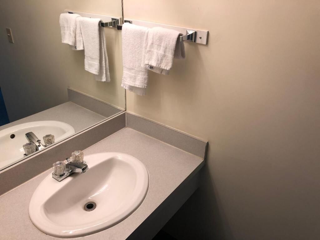 Ein Badezimmer mit einem weißen Waschbecken, einem Spiegel und einem Handtuchhalter mit weißen Handtüchern.