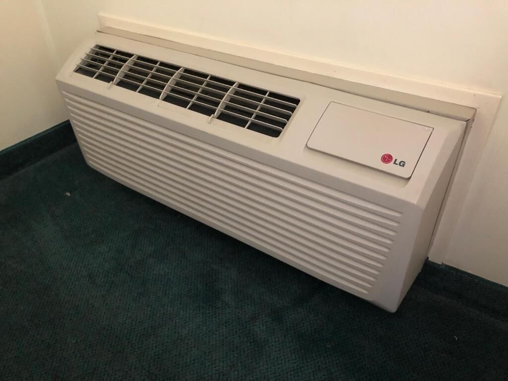 A white LG air conditioner unit with a control panel and vents, placed on a dark carpeted floor.