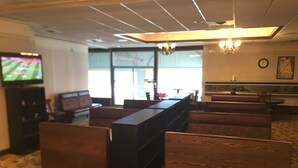 Un hall de hotel con piso alfombrado, mobiliario de madera, un televisor, una araña y un reloj en la pared.