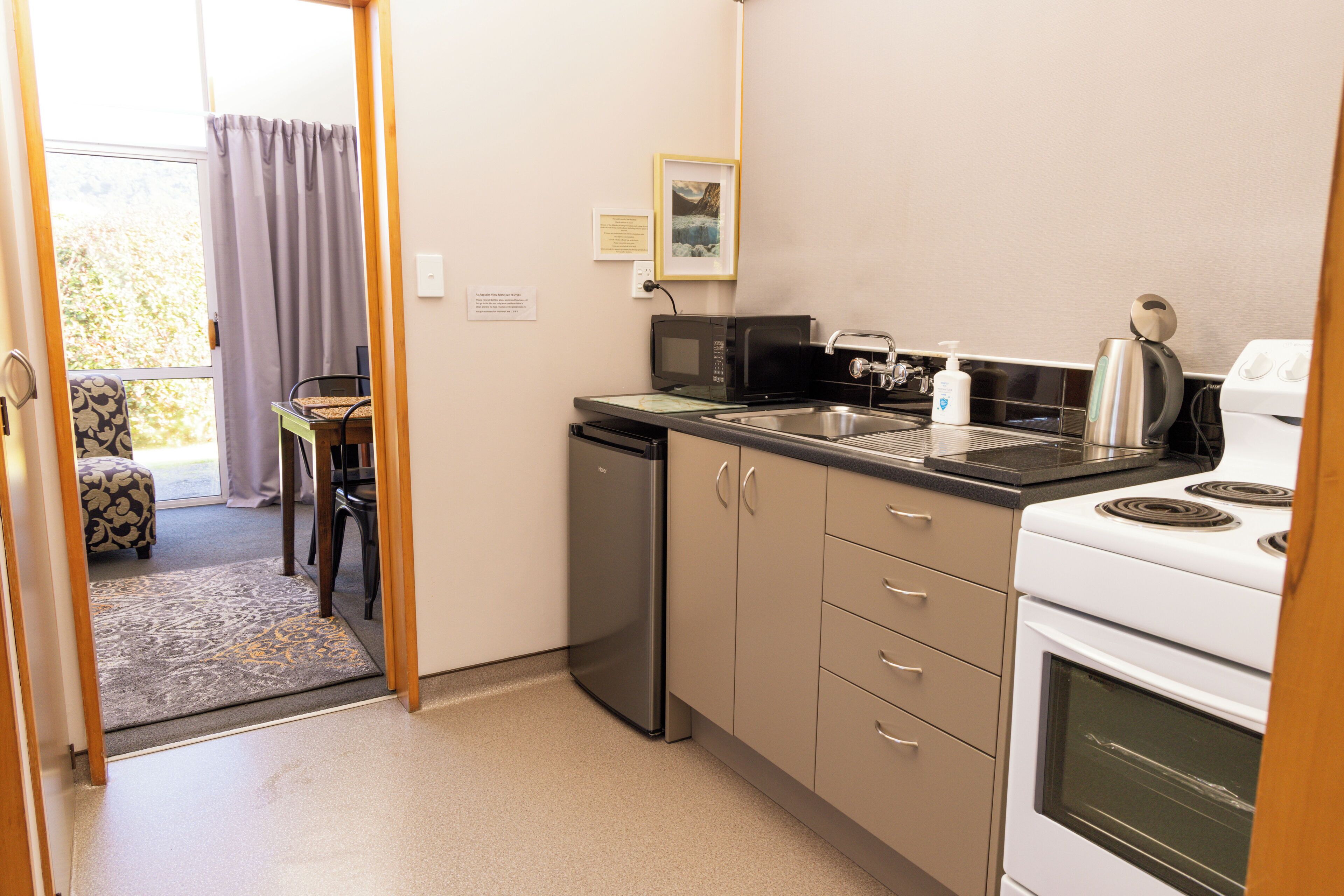 A compact kitchen with a microwave, sink, and stove. There is a small dining area with a chair and table.