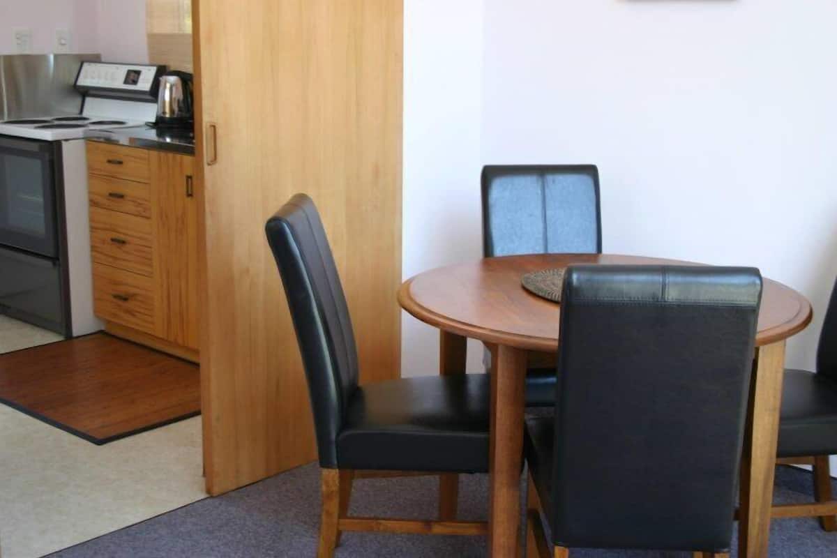 A compact kitchen with a stove, microwave, and a coffee maker. There is a wooden cabinet with drawers and a door. The room has a round wooden table with four black chairs.