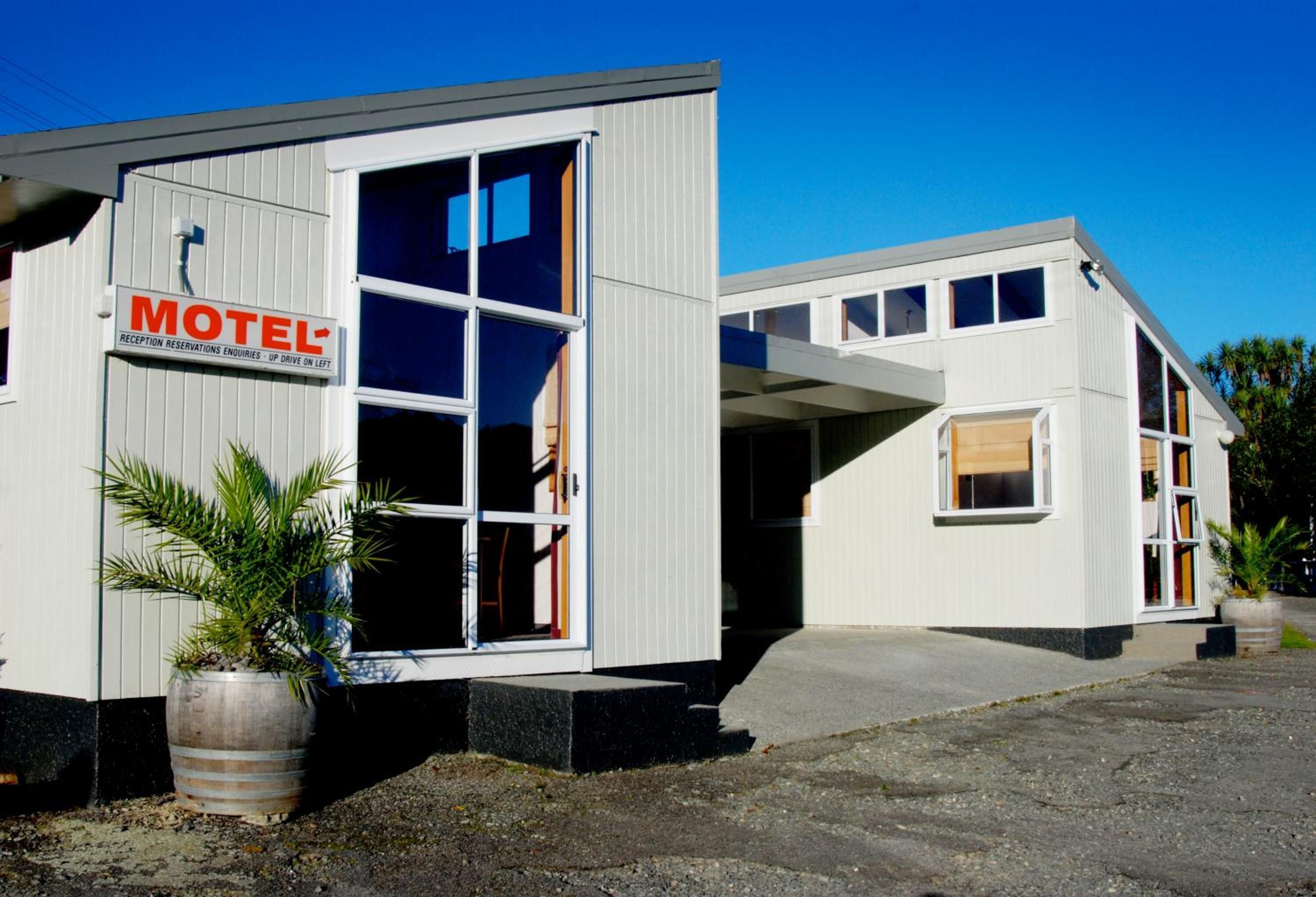 A motel with a signboard, a large window, and a potted plant.