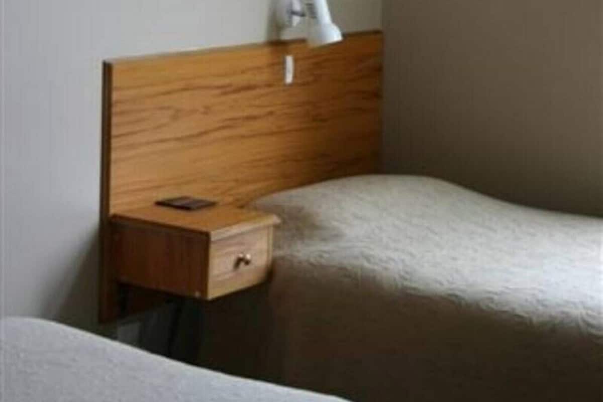 A hotel room with two beds, a wooden headboard, a nightstand, and a lamp.