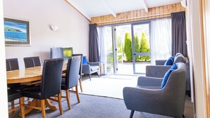 A conference room with a wooden table and chairs, a sofa, and a large window with curtains. - Apostles View Motel (Greymouth)