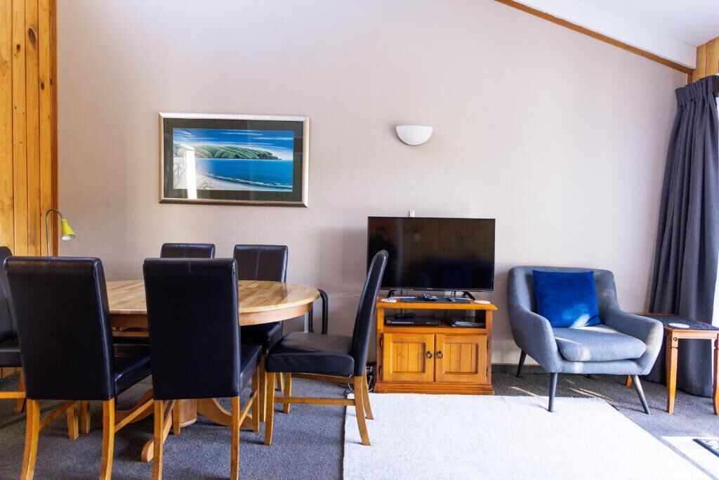 A room with a round dining table, chairs, a television, a cabinet, and a framed picture on the wall.