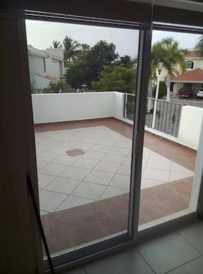 A balcony with a tiled floor, a white railing, and a view of a residential area with houses and trees.