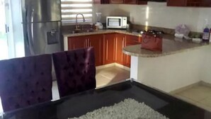 A kitchen with wooden cabinets, a stainless steel refrigerator, a microwave, and a dining area with a table and chairs.