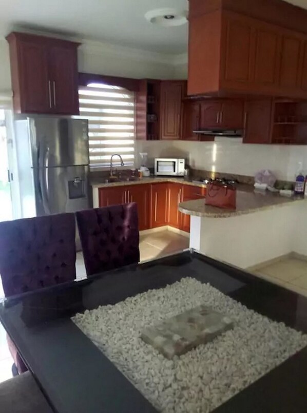 A kitchen with wooden cabinets, a stainless steel refrigerator, a microwave, and a dining area with a table and chairs.