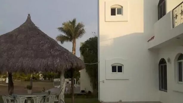 A building with a white exterior, a thatched-roof structure, and a small garden area with a table and chairs.