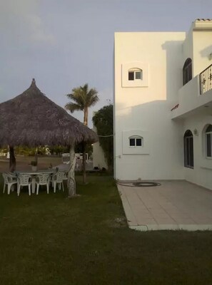 A building with a white exterior, a thatched-roof structure, and a small garden area with a table and chairs.