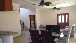 A spacious living area with a dining table, purple chairs, a sofa, and two ceiling fans.